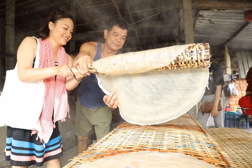 Les touristes expérimentent la cuisson et le séchage des papiers de riz. Photo: Vietnam+ 