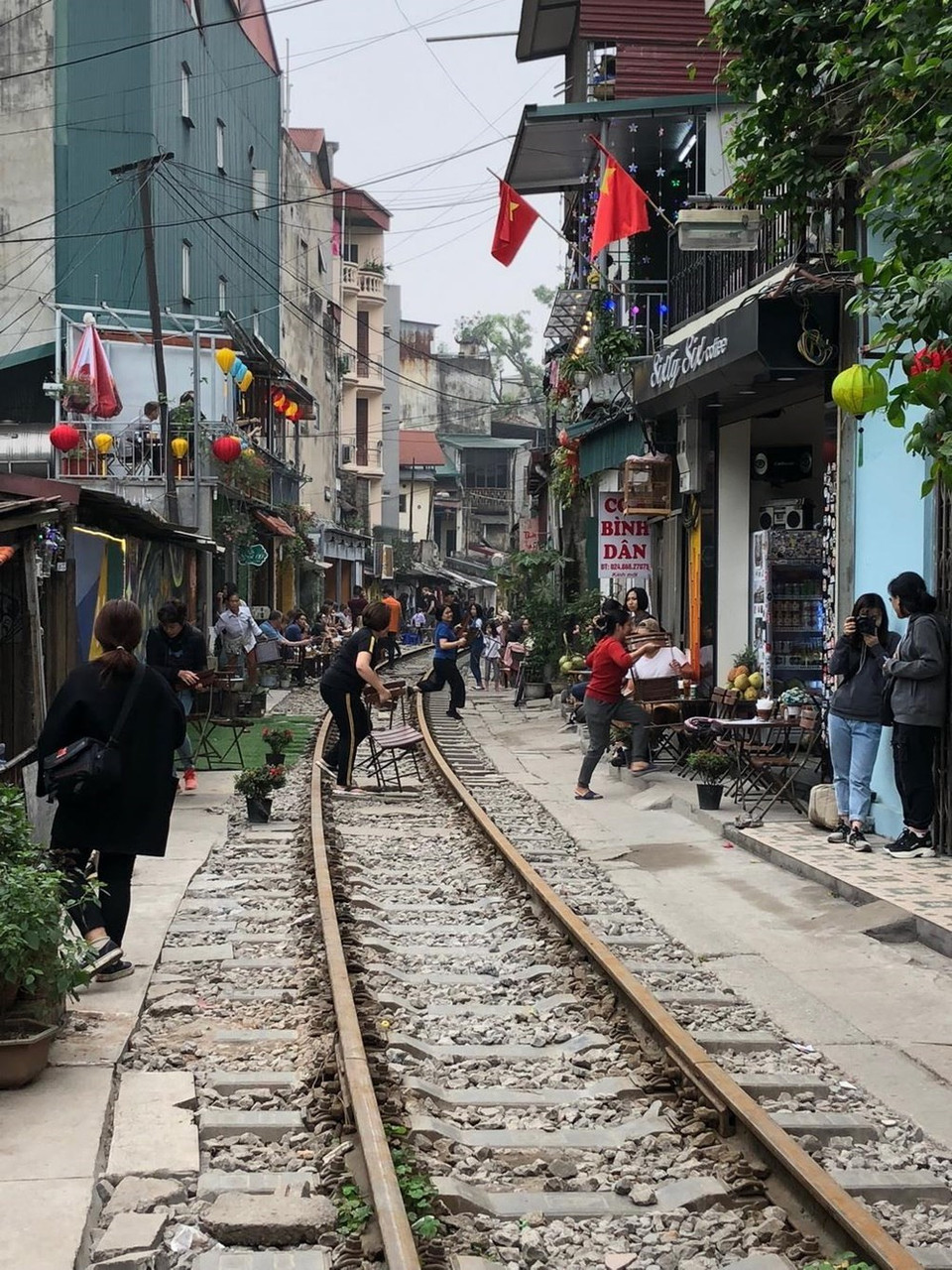 Quand le train arrive, les touristes et les habitants déplacent leurs tables et leurs tabourets pour sortir de la voie