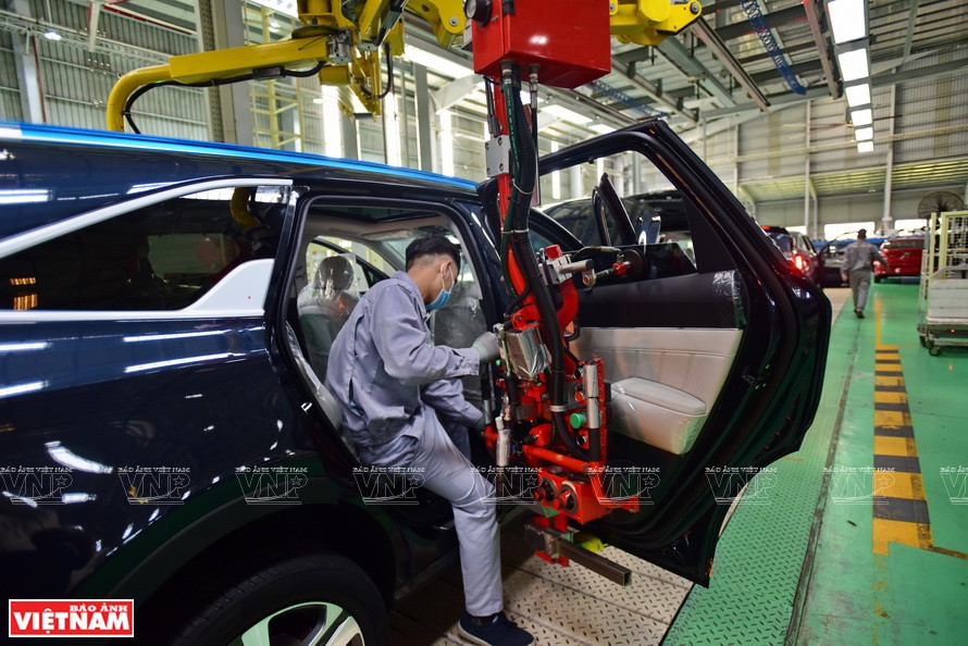 Des ouvriers utilisent des bras robotisés pour assembler les portes des voitures.