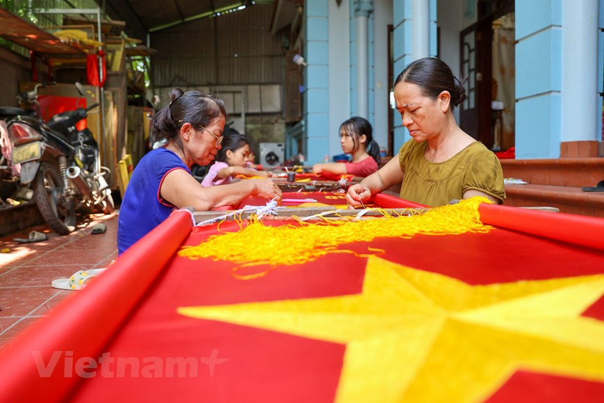 Au cours de la dernière décennie, la demande de drapeaux nationaux a augmenté et sa famille est devenue plus occupée en conséquence. À l'approche des événements nationaux, le drapeau national (un drapeau rouge avec une étoile jaune à cinq branches au centre) est en forte demande et les villageois de Tu Van entrent au sommet de leur production de drapeau. Pour un brodeur vétéran comme Vuong Thi Nhung, il faut souvent entre 3 et 5 jours pour terminer la broderie d'un drapeau. Pour les amateurs, cela peut prendre jusqu'à une semaine. Broder le drapeau national est un travail exigeant qui demande beaucoup de finesse et de minutie dans chaque point, car les produits finaux sont pour des événements importants. Photo: VietnamPlus