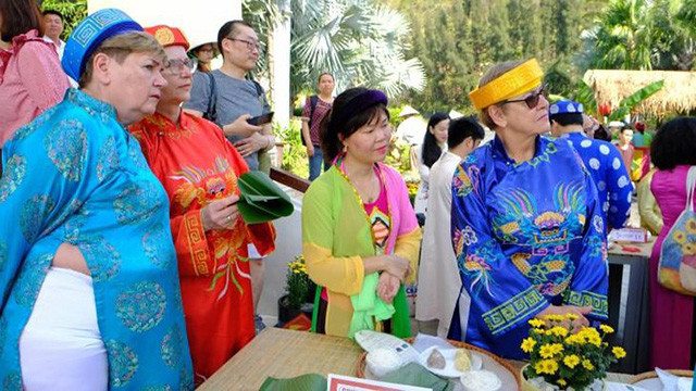 Les visiteurs étrangers en costumes traditionnels vietnamiens participent à la préparation des « banh chung