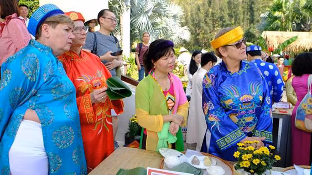 Les visiteurs étrangers en costumes traditionnels vietnamiens participent à la préparation des « banh chung