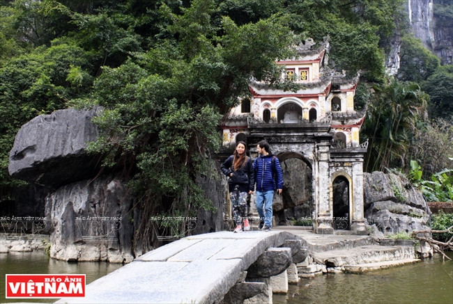 Un pont de pierre sculpté de motifs en forme de tête de dragon mène au porche de la pagode Bich Dông.
