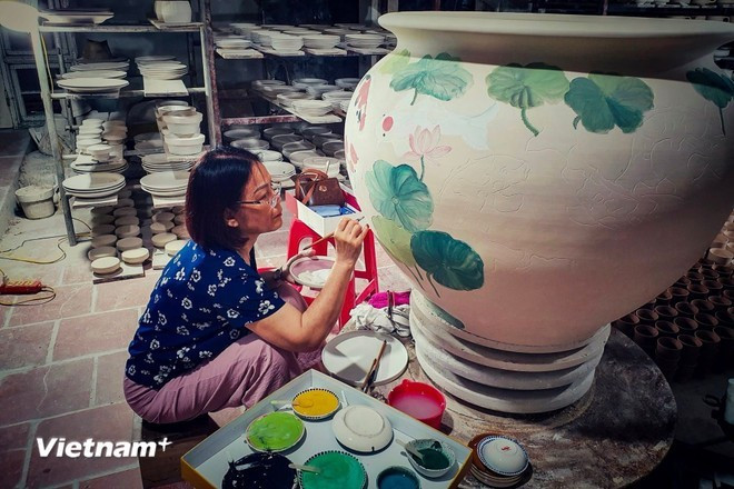 L'artisane Pham Thi Minh Chau peint méticuleusement des motifs sur un produit en céramique de Bat Trang. Photo : VietnamPlus chau.jpg