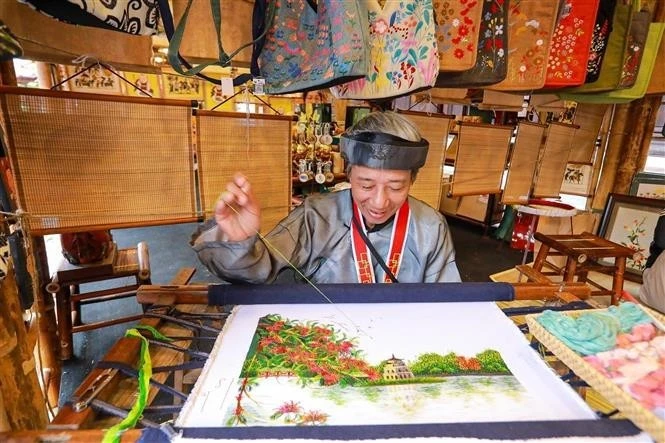 Un artisan brode une peinture dans l'espace d'exposition. Photo : VNA.