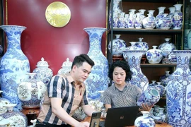 L’artisan Trân Trung Hiêu, dans la commune de Bat Tràng, district de Gia Lâm, à Hanoi, partage avec sa collègue sur la manière d’introduire des céramiques sur les plateformes de commerce électronique. Photo : NDEL
