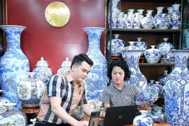 L’artisan Trân Trung Hiêu, dans la commune de Bat Tràng, district de Gia Lâm, à Hanoi, partage avec sa collègue sur la manière d’introduire des céramiques sur les plateformes de commerce électronique. Photo : NDEL
