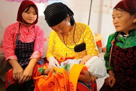 Une sage-femme prend un bébé dans ses bras sous le regard attentif de sa mère. Photo: VNA