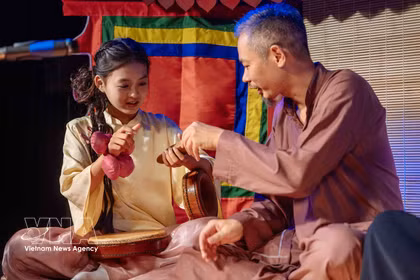Une jeune s’initie à un instrument de musique auprès d'un artisan. Photo : VNA