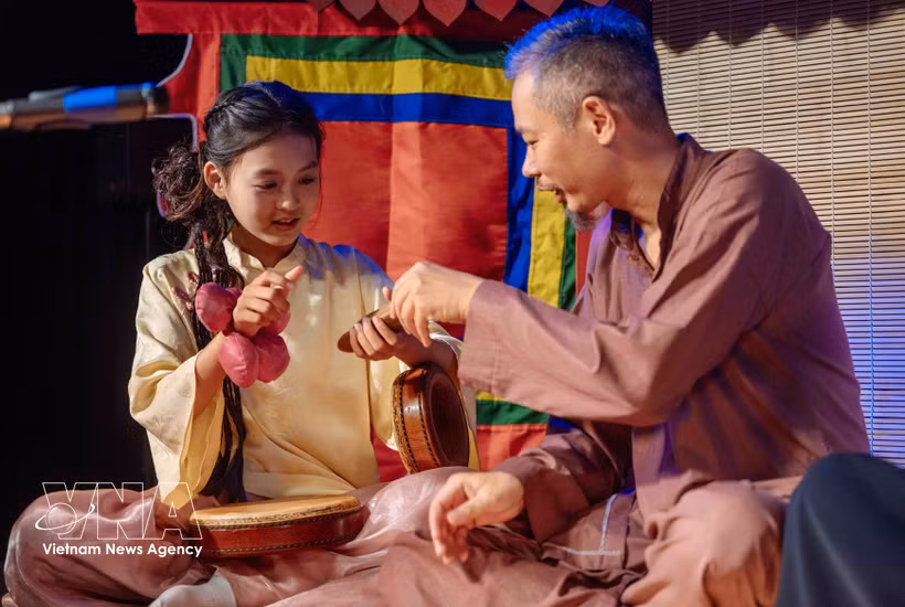 Une jeune s’initie à un instrument de musique auprès d'un artisan. Photo : VNA