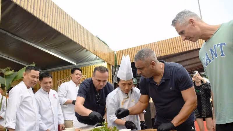 Des touristes internationaux découvrent la préparation de salades de poisson au Festival gastronomique de Dà Nang 2025. Photo: NDEL