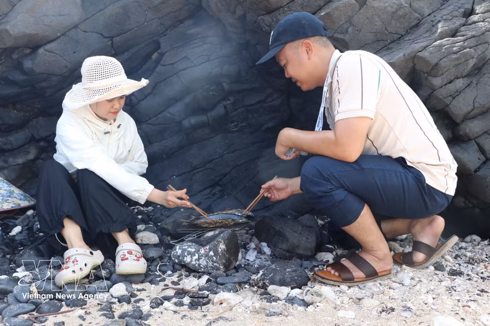 Les visiteurs profitent d’un moment de convivialité en dégustant des poissons grillés directement sur le rivage. Photo : VNA