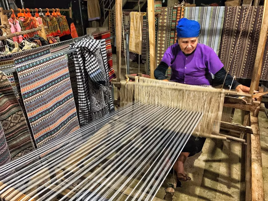 Les touristes peuvent regarder des femmes locales tisser des produits de brocart tels que sacs à main, sacs et foulards piêu (foulard traditionnel de l’ethnie Thai). Le tissage de brocart est l'artisanat traditionnel qui crée des caractères culturels qui fascinent les touristes se rendant au village de Lac dans le district de Mai Chau, dans la province septentrionale de Hoa Binh. Une caractéristique culturelle inhabituelle du peuple Thai est clairement visible à travers leurs costumes: un foulard qui traverse la tête, une chemise bleue et une jupe noire au sol. Les filles portent souvent une pièce en brocart qui traverse sa poitrine qui les aide à paraître gracieuses. Photo: Vietnam+