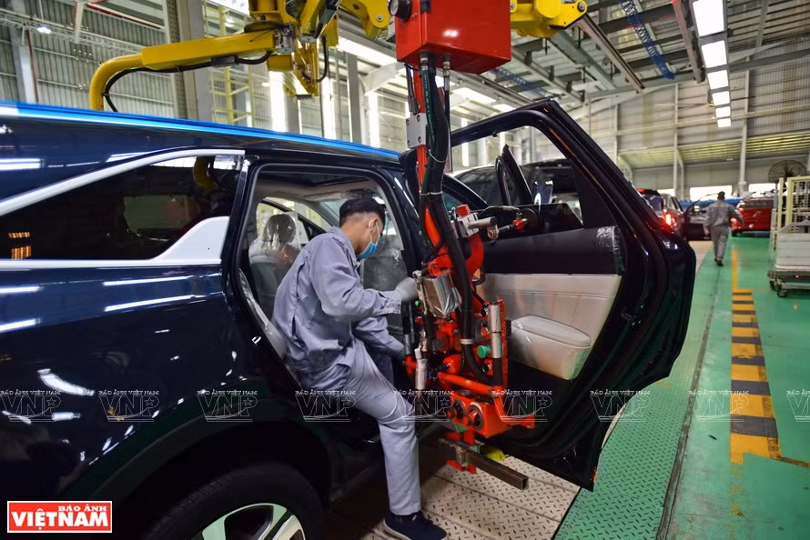 Des ouvriers utilisent des bras robotisés pour assembler les portes des voitures.