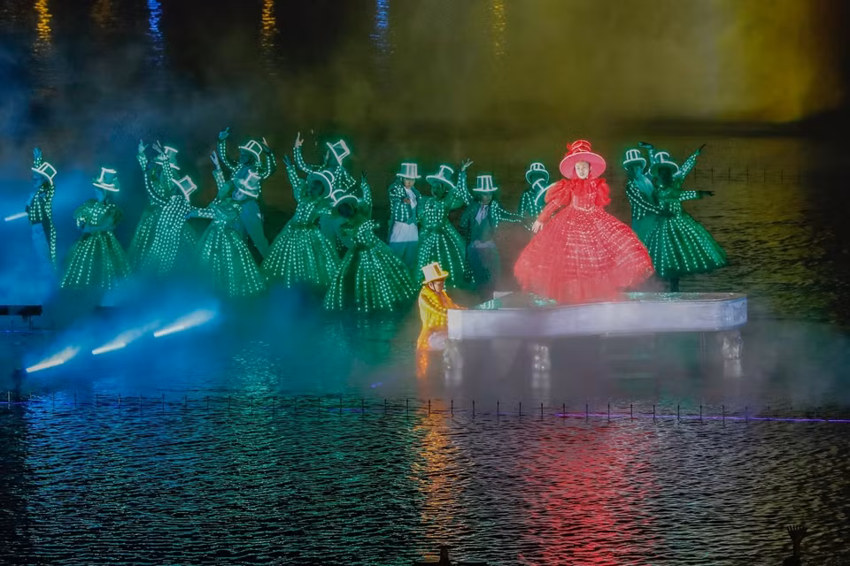 Des artistes masqués, vêtus de costumes sophistiqués équipés de lumières LED, se produisent sur une scène flottante au milieu de l'eau, créant une atmosphère de carnaval à Venise. 