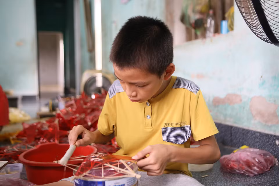 Un enfant du village de Bao Dap aide ses parents à fabriquer des lanternes.